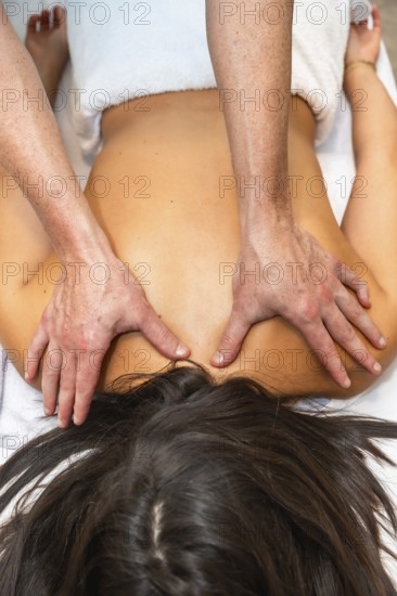 Therapist hands applying pressure to a woman's shoulders and upper back while she is lying on a towel covered massage table, focusing on relaxation and relieving muscle tension