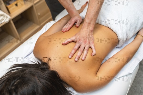 Young woman lying on spa table receiving therapeutic back massage from professional masseur, hands easing muscle tension for relaxation, healing and overall wellness