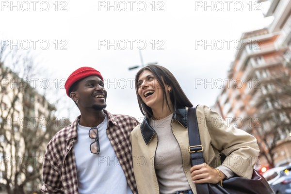 Young diverse couple walking and laughing on a city street, sharing a joyful, candid moment of connection, friendship and relaxed, stylish urban togetherness