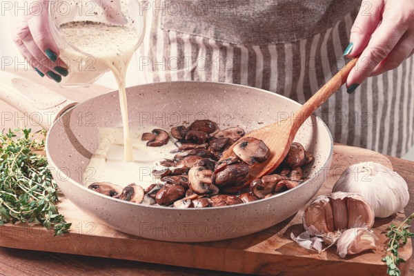 Cooking sauce with mushrooms, a woman pours cream into a pan with mushrooms, natural light, lifestyle