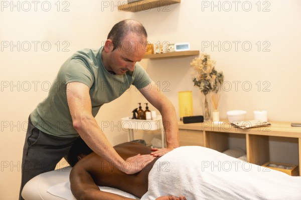 Professional male masseur concentrating while giving a deep tissue back massage to a client lying on a treatment table in a serene spa or wellness center setting