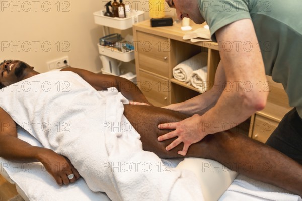 African american man lying on a table enjoying a professional leg massage provided by a therapist for relaxation, muscle recovery, and physical therapy in a calm spa environment