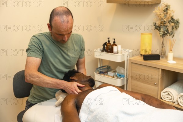 Male therapist applying therapeutic pressure to a male client's neck and shoulders on a massage table, promoting relaxation and physical wellness in a modern treatment room