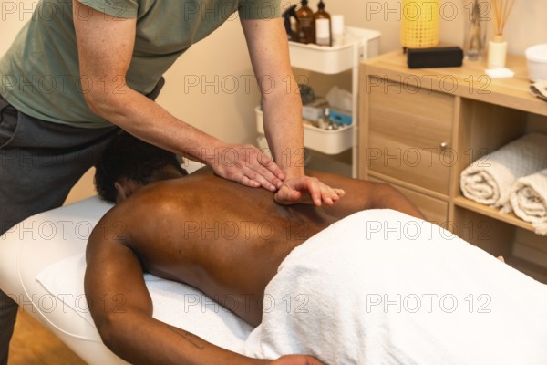 Skilled masseur using hands and elbow to apply deep tissue treatment on the back of a male client, promoting muscle relaxation and wellness in a spa setting