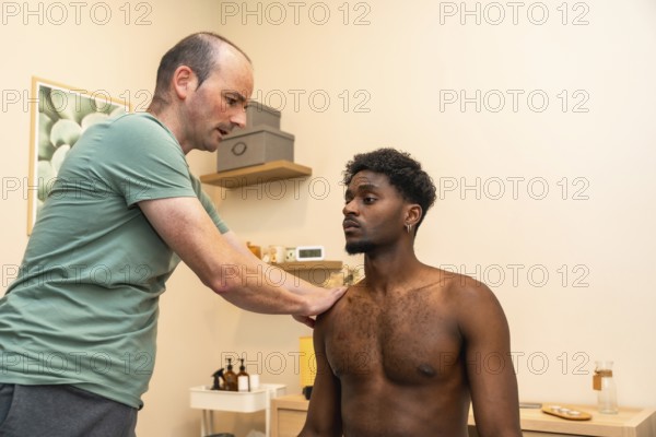Male practitioner examining a young man's shoulder, providing professional medical care during a chiropractic session or physiotherapy treatment in a modern clinic setting