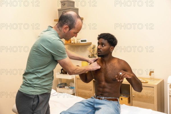 Physical therapist performing an examination and palpation on a young adult male patient's shoulder during a rehabilitation session in a professional clinic setting