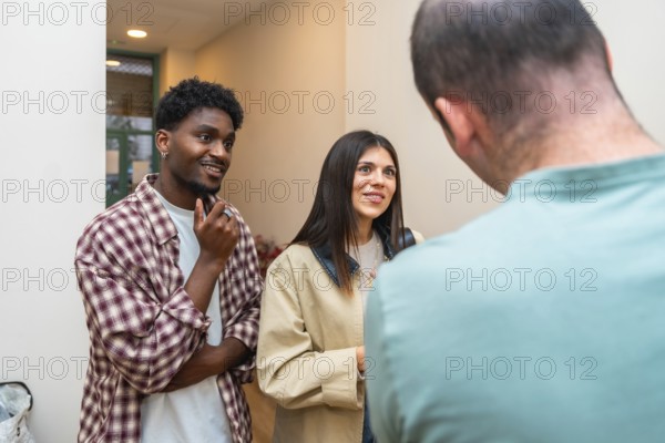Diverse group of three young adults connecting in a casual indoor setting, actively listening and smiling while engaging in friendly social communication