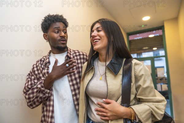 Two young adults, a black man and a caucasian woman, engaging in a lively conversation, sharing a laugh, and walking through an indoor urban setting, expressing genuine connection and happiness