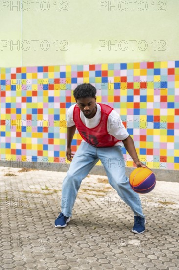 Young man dribbling a colorful basketball on a pavement court, showcasing an active street sport lifestyle against a vibrant, patterned wall reflecting energy and youth