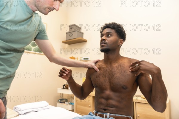 Male physiotherapist examining a young adult patient's shoulder and upper body, assessing mobility and identifying the source of muscle pain during a rehabilitation session