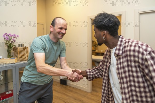 Two men from different backgrounds smiling and shaking hands in an office, symbolizing friendly partnership, trust, collaboration and successful multicultural business connection