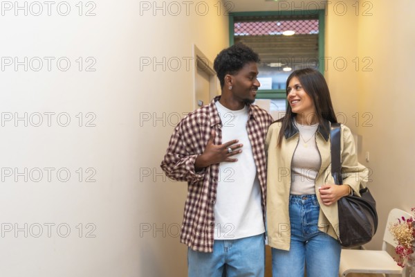 Young intercultural couple walking indoors, smiling and looking at each other with joy and connection, sharing a candid, modern moment of intimacy and togetherness in home setting