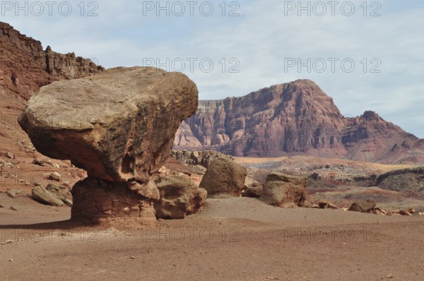 A gigantic rock sits on red desert sand in front of a barren rocky landscape, Grand Canyon National Park, Arizona, USA