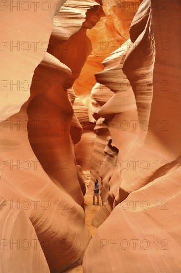 A traveler explores the narrow, winding passages of an orange slot canyon, Antelope Canyon, Navajo Nation Reservation, Lake Powell Tribal Park, Arizona, USA