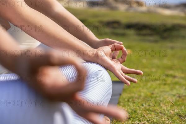 Woman forming a meditative mudra with hands while seated on green grass, focusing on inner peace, mindfulness and calm during outdoor yoga practice in daylight