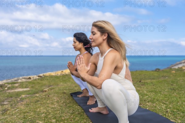 Two women performing a yoga pose and meditating outdoors, finding wellness and spiritual harmony in nature by the ocean, connecting with mindfulness and inner peace