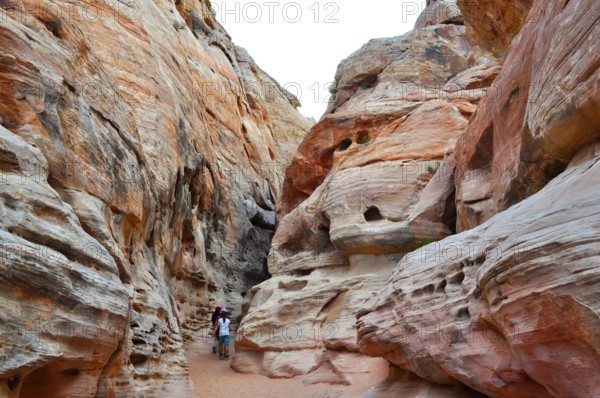 Narrow canyon with huge red rock walls and hikers, Valley of Fire State Park, Nevada, USA