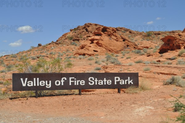 Valley of Fire State Park sign against a red rocky landscape under a blue sky, Valley of Fire State Park, Nevada, USA