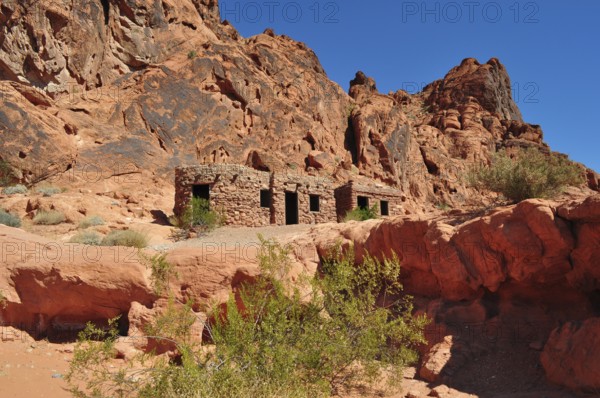 Abandoned stone houses nestled in a red rocky landscape under clear skies, Valley of Fire State Park, Nevada, USA