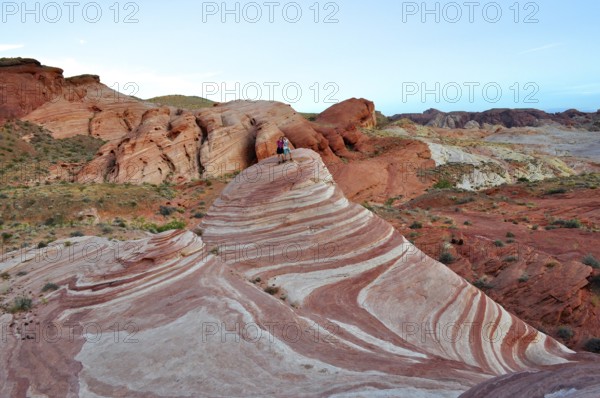 Two people standing on a striped rock formation in a desert landscape, Valley of Fire State Park, Nevada, USA