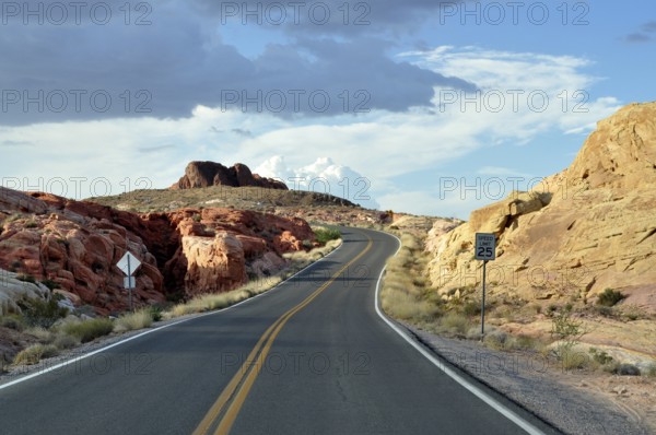 Narrow road with road sign snakes through red rocks under dramatic clouds in the sky, Valley of Fire State Park, Nevada, USA