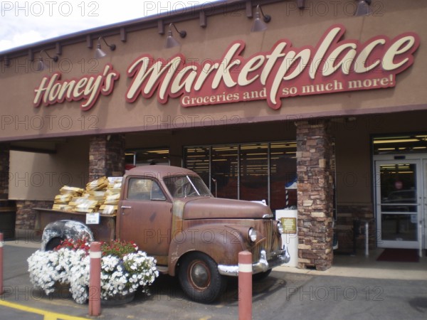 Old Studebaker pickup truck full of flowers parked in front of a nostalgic market building, Honey's Marketplace, Moab, Utah, USA