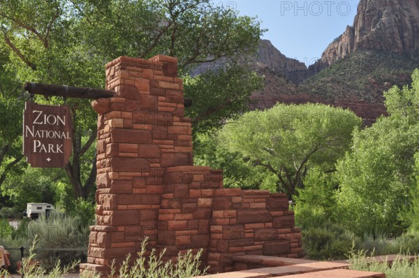 Brick monument with sign in Zion National Park, surrounded by green trees and mountains, Zion National Park, Utah, USA