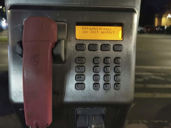 Public telephone at night, display shows error message, sorry currently disturbed, urban area, Berlin