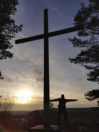 A large cross and a silhouette of a person at sunset, view over Kronach from Kreuzberg, Frankenwald nature park Park