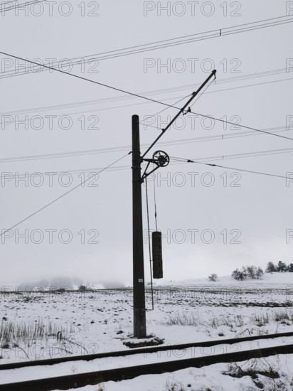 Snow-covered landscape with power pole and power lines on snow-covered railway tracks, Thuringian Forest nature park Park