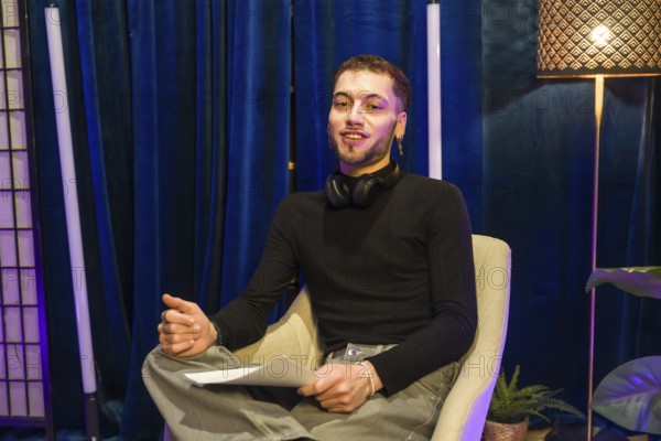 Young man wearing headphones around his neck and holding papers. Actively engaging. Communicating. And presenting while recording a video for social media or a podcast in a professional studio setting