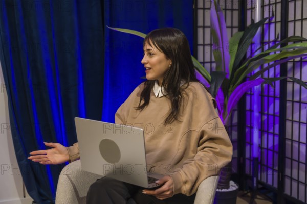 Woman presenting ideas from a modern content creation studio, smiling and gesturing while recording a podcast or livestream with laptop and professional lighting setup