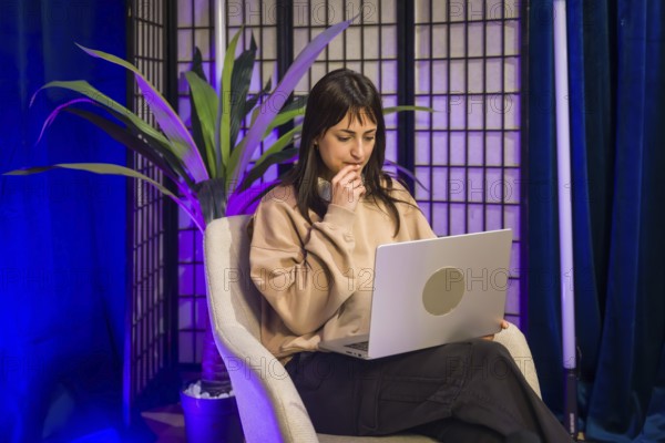 Young woman focused at a laptop in a modern studio, planning and creating social media and podcast content for online audiences, remote work and digital entrepreneurship