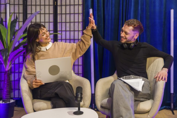 Two smiling content creators high fiving during a successful recording session in a modern podcast studio, collaborating on audio content and social media projects