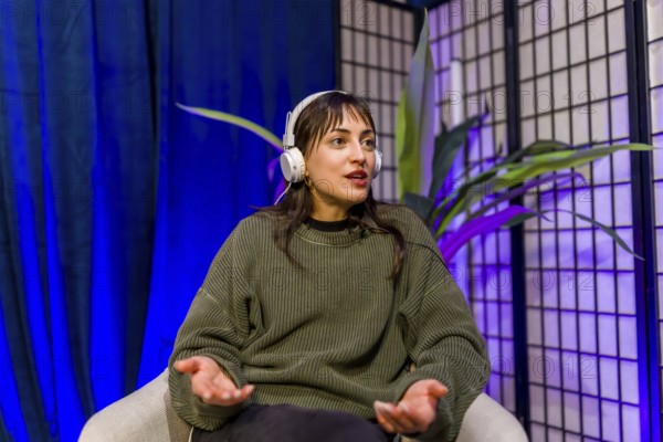 Woman wearing headphones and gesturing while speaking, creating engaging audio content for social media or a podcast in a professional recording studio