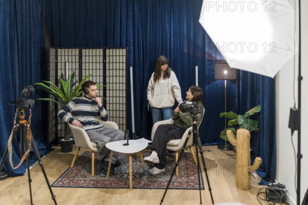 Content creators producing new social media video, with two people sitting and discussing while a young woman stands behind them, using professional recording equipment