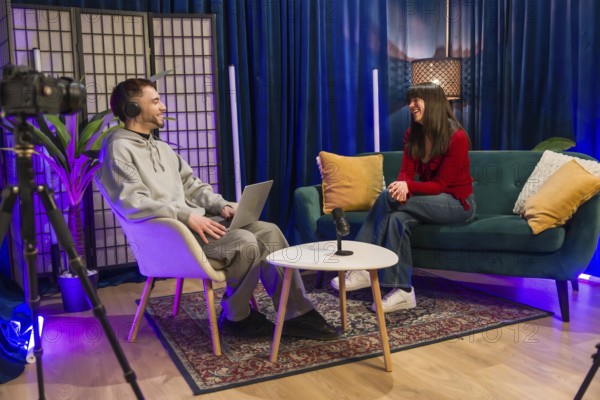 Diverse young content creators recording a podcast or social media video, sitting in a modern studio setup with microphone, laptop, and camera equipment