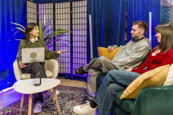 Young diverse creators recording a podcast in a stylish studio, chatting around microphones and laptops, collaborating on digital content for streaming and social media audiences