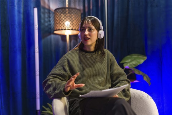 Young woman recording social media content or a podcast episode, wearing headphones and holding notes while discussing a topic in a modern studio environment