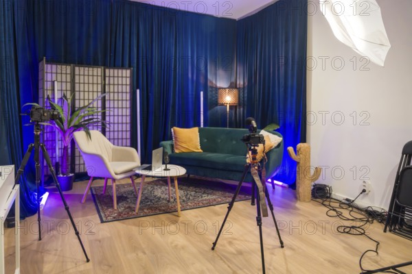 Modern content creation studio set up for video recording and podcast production, featuring cameras, microphones, lighting, and a comfortable seating area against blue curtains