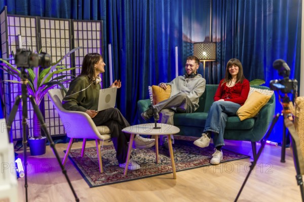 Three young content creators engaging in a conversation, recording a podcast or social media video interview in a modern studio equipped with cameras and microphones for broadcasting