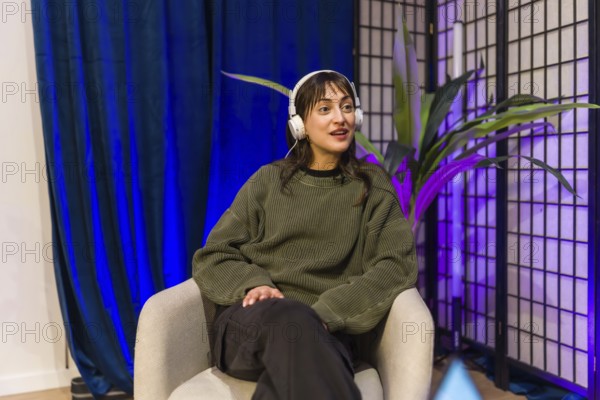 Young woman in a modern home studio wearing headphones, hosting a podcast or livestream, speaking into a mic while recording audio and engaging an online audience