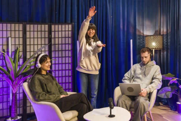 Young adults collaborating in a modern home studio, recording a podcast and creating video content with microphones, laptops and colorful lighting for social media and streaming platforms