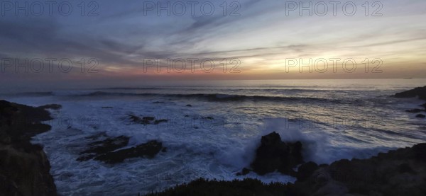 Dramatic sunset with dark clouds and waves, rocks in the foreground, hiking on the Fisherman's Trail, Southwest Alentejo nature park Park and Vicentina Coast, Portugal