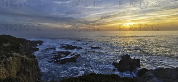 The golden sun sets over the vast sea, illuminated by bright clouds, hiking on the Fisherman's Trail, Algarve, Portugal