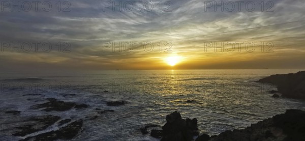 The picture shows an atmospheric sunset over the sea with dramatic clouds, hiking on the Fisherman's Trail, Algarve, Portugal