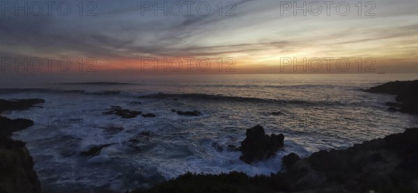 Subdued sunset with dark clouds and rocks in the sea, romantic atmosphere, hiking on the Fisherman's Trail, Southwest Alentejo nature park Park and Vicentina Coast, Portugal