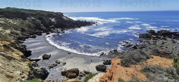 A rocky stretch of coast with a view of the blue sky and the rushing sea, hiking on the Fisherman's Trail, Algarve, Portugal