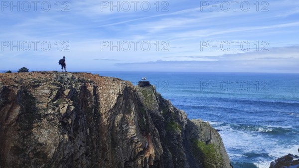 Lone hiker on rocky cliff overlooking the vast ocean, stork's nest (ciconia), Fisherman's trail, Algarve, Portugal