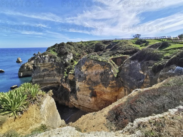 Rocky cliffs with lush vegetation and blue sea under a cloudy sky, Lagos, Algarve, Portugal